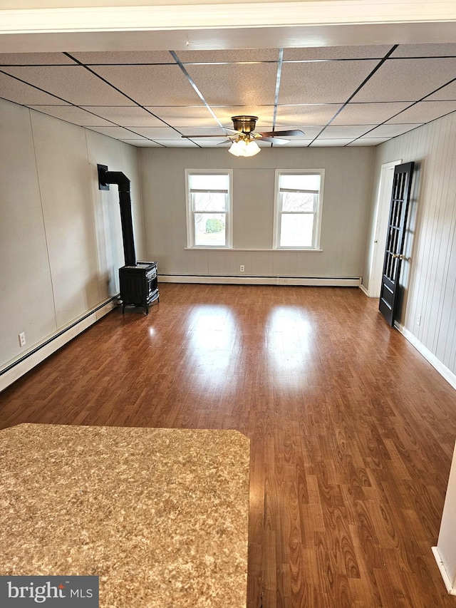 interior space featuring wood finished floors, a drop ceiling, a wood stove, and a ceiling fan