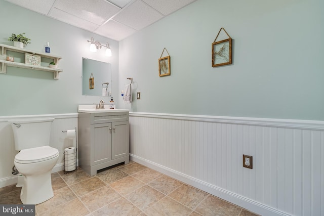 half bathroom with a wainscoted wall, vanity, toilet, and a paneled ceiling
