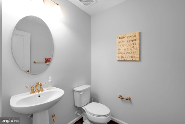 bathroom with baseboards, toilet, a sink, and visible vents