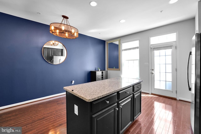 kitchen featuring dark wood-style flooring, a chandelier, dark cabinetry, a kitchen island, and refrigerator