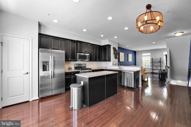 kitchen with a sink, a chandelier, appliances with stainless steel finishes, dark cabinets, and a kitchen island