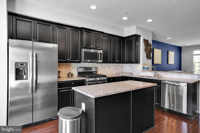 kitchen featuring dark wood finished floors, stainless steel appliances, dark cabinets, a sink, and a kitchen island