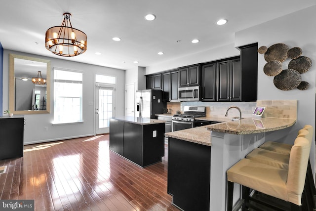 kitchen with tasteful backsplash, a chandelier, dark cabinetry, appliances with stainless steel finishes, and a kitchen island