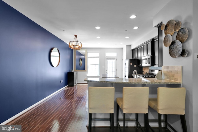 kitchen featuring a kitchen breakfast bar, a peninsula, baseboards, appliances with stainless steel finishes, and recessed lighting