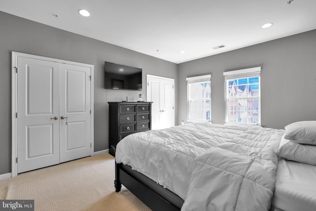 bedroom featuring light carpet, multiple closets, visible vents, and baseboards