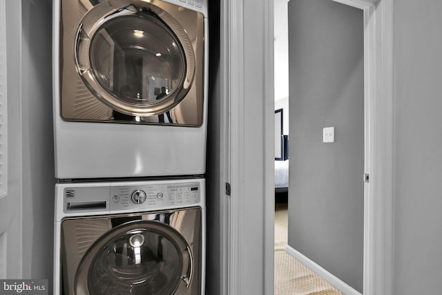 washroom with baseboards, stacked washer and clothes dryer, and laundry area