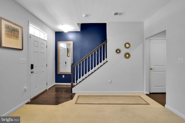 carpeted entryway featuring baseboards, wood finished floors, visible vents, and stairway