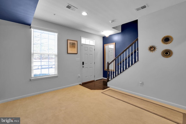 foyer entrance featuring carpet, visible vents, baseboards, and stairs