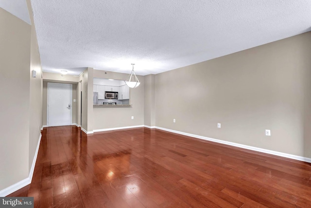 unfurnished living room with baseboards, dark wood-style flooring, and a textured ceiling