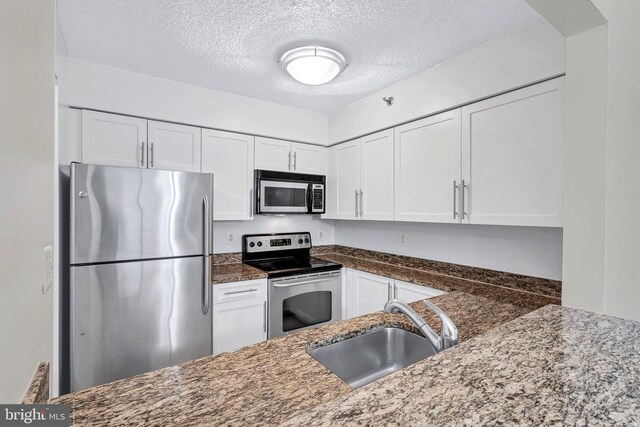 kitchen with a sink, white cabinetry, appliances with stainless steel finishes, a textured ceiling, and dark stone counters