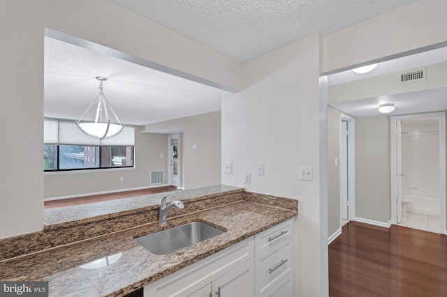 kitchen featuring a textured ceiling, a sink, stone countertops, visible vents, and white cabinets