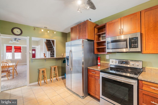 kitchen featuring stainless steel appliances, light tile patterned floors, open shelves, a ceiling fan, and light stone counters