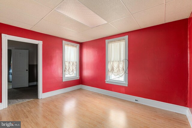 spare room with wood finished floors, a paneled ceiling, and baseboards
