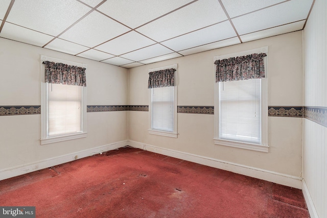 carpeted empty room with plenty of natural light, a paneled ceiling, and baseboards