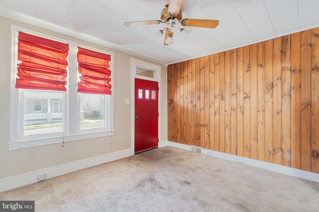 carpeted entryway featuring wooden walls, a ceiling fan, visible vents, and baseboards