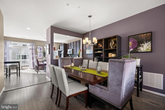 dining room featuring hardwood / wood-style floors, an inviting chandelier, baseboards, and visible vents