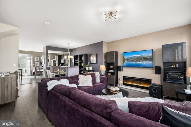 living room featuring an inviting chandelier, a glass covered fireplace, and dark wood finished floors