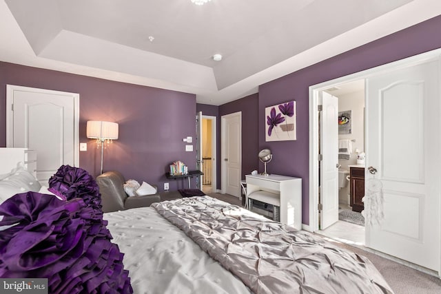 bedroom with a tray ceiling, carpet, and connected bathroom