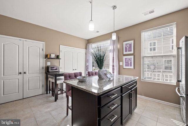 kitchen featuring freestanding refrigerator, visible vents, light tile patterned flooring, hanging light fixtures, and a breakfast bar area