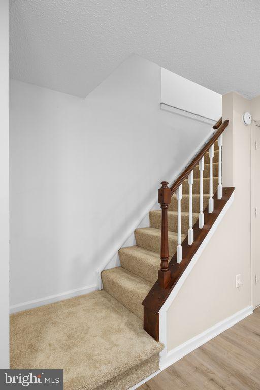 staircase with wood finished floors, baseboards, and a textured ceiling