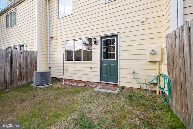 property entrance featuring central AC unit, a lawn, and fence