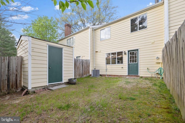 rear view of property with an outbuilding, a lawn, a fenced backyard, a storage unit, and a chimney