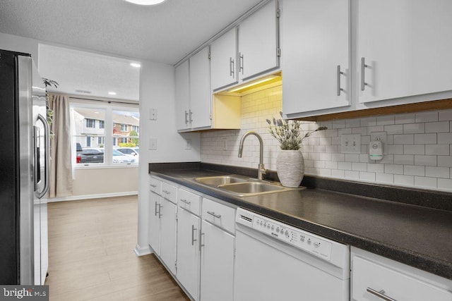 kitchen featuring stainless steel fridge, backsplash, a sink, dark countertops, and dishwasher