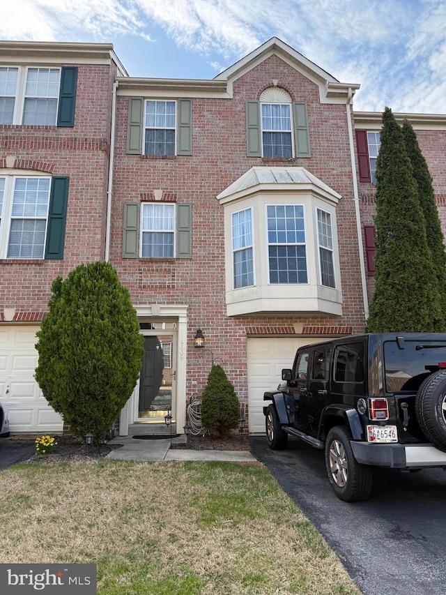 townhome / multi-family property with driveway, brick siding, a front lawn, and a garage