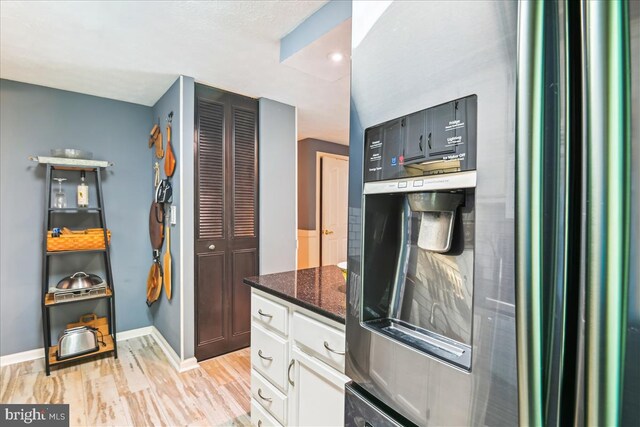 kitchen with white cabinets, dark stone countertops, baseboards, light wood-type flooring, and stainless steel refrigerator with ice dispenser