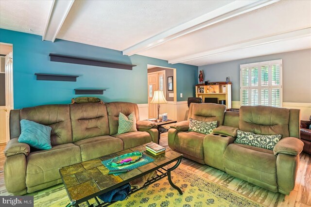 living area with wood finished floors, beam ceiling, and a wainscoted wall