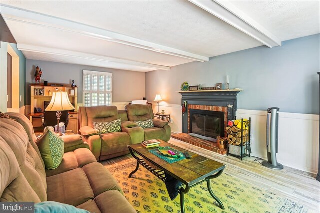 living area with a wainscoted wall, wood finished floors, a fireplace, and beamed ceiling