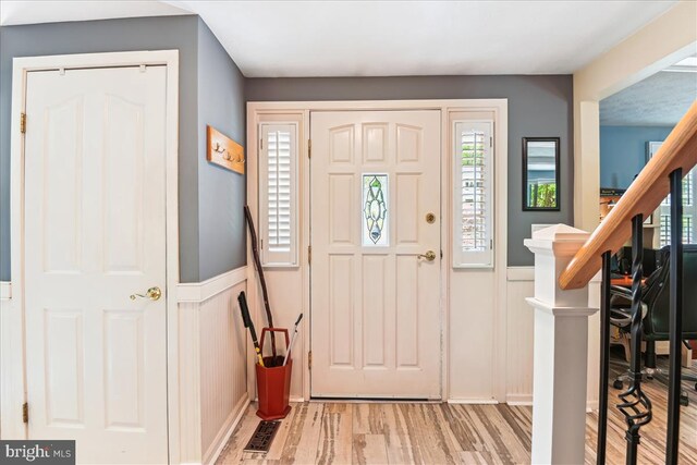 foyer entrance with a wainscoted wall, light wood-type flooring, and visible vents
