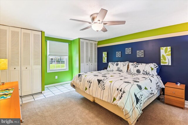 carpeted bedroom featuring a ceiling fan, multiple closets, and tile patterned floors