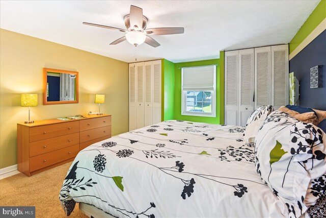 carpeted bedroom with a ceiling fan and two closets