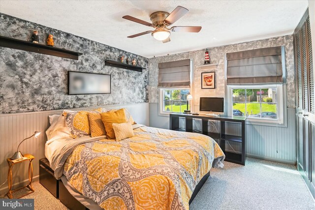 bedroom with carpet floors, a textured ceiling, wainscoting, and a ceiling fan