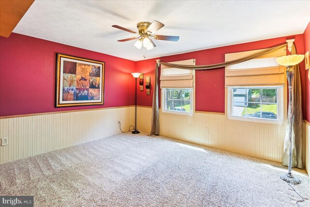 carpeted empty room featuring ceiling fan and a wainscoted wall