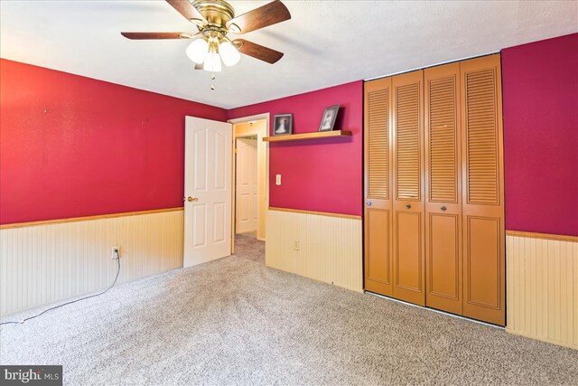 unfurnished bedroom with a closet, wood walls, a wainscoted wall, a ceiling fan, and carpet