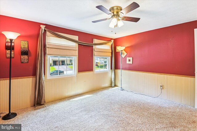 carpeted empty room with a ceiling fan and a wainscoted wall