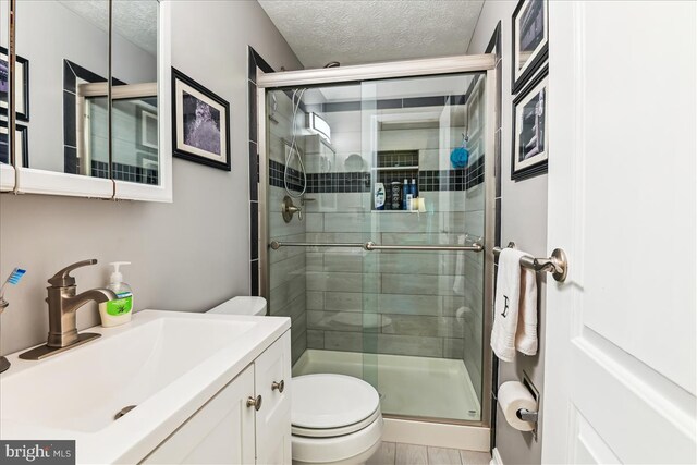 bathroom featuring vanity, a textured ceiling, a stall shower, and toilet
