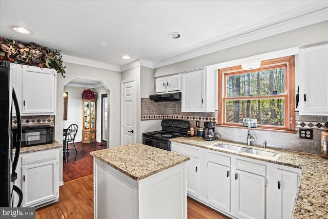 kitchen with arched walkways, a sink, under cabinet range hood, black appliances, and dark wood-type flooring