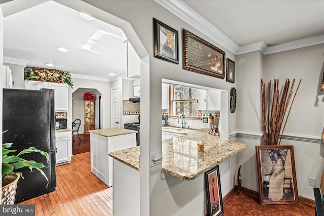 kitchen with ornamental molding, a peninsula, light wood-style flooring, a center island, and freestanding refrigerator