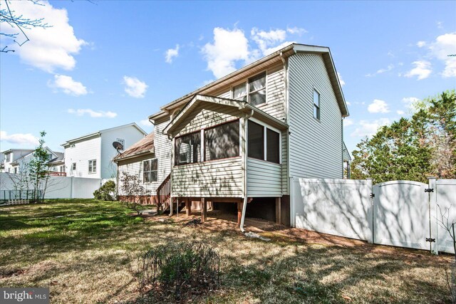 rear view of house with a sunroom, a yard, fence, and a gate