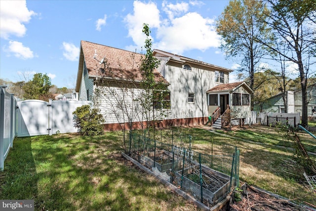rear view of house featuring a fenced backyard, a gate, a lawn, and a vegetable garden