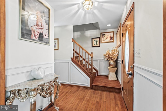 entrance foyer featuring hardwood / wood-style floors, a decorative wall, wainscoting, and stairway