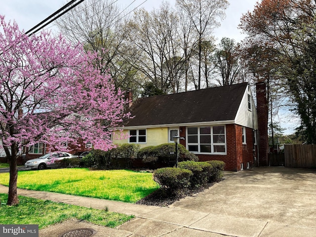 view of front of home featuring a front yard, concrete driveway, a chimney, fence, and brick siding