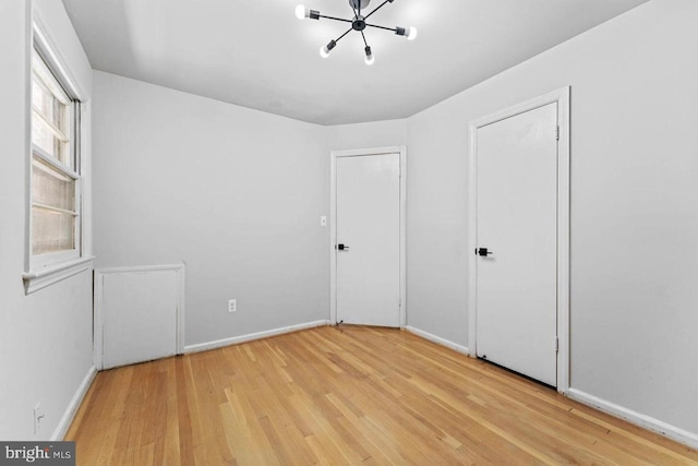 unfurnished bedroom featuring baseboards, light wood-type flooring, and an inviting chandelier