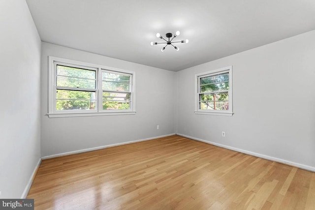 empty room with an inviting chandelier, baseboards, and light wood-type flooring