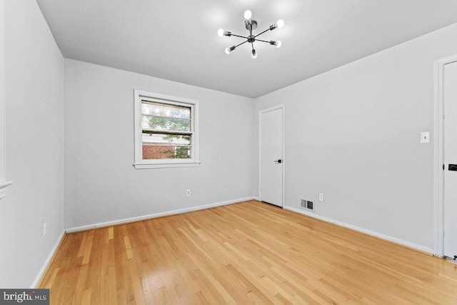 spare room with an inviting chandelier, baseboards, light wood finished floors, and visible vents