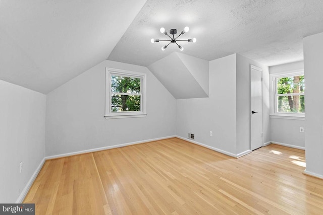 bonus room with baseboards, lofted ceiling, a textured ceiling, and light wood-style flooring