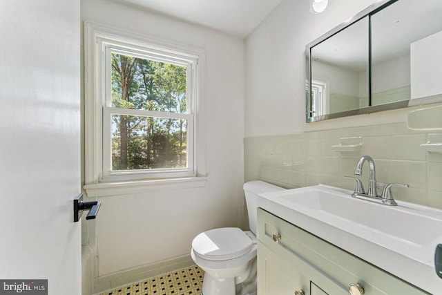 half bath with toilet, a wainscoted wall, tile walls, and vanity